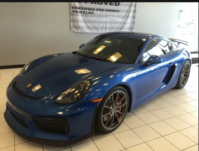 Blue Porsche sports car displayed in a showroom with a certified pre-owned vehicles banner visible