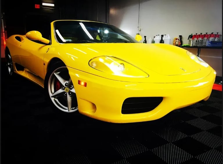 Bright yellow Ferrari sports car displayed in a garage showroom with headlights on
