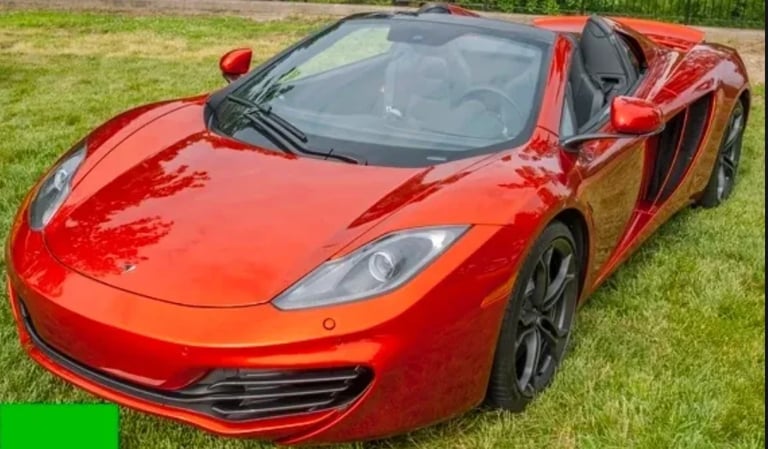 Bright red sports car with open drivers side door parked on grass