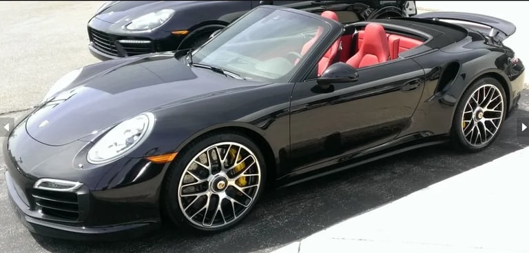 Black Porsche 911 convertible sports car with red interior and gold wheels parked outdoors
