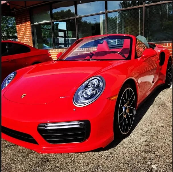 Bright red Porsche sports car parked outside brick building with large windows