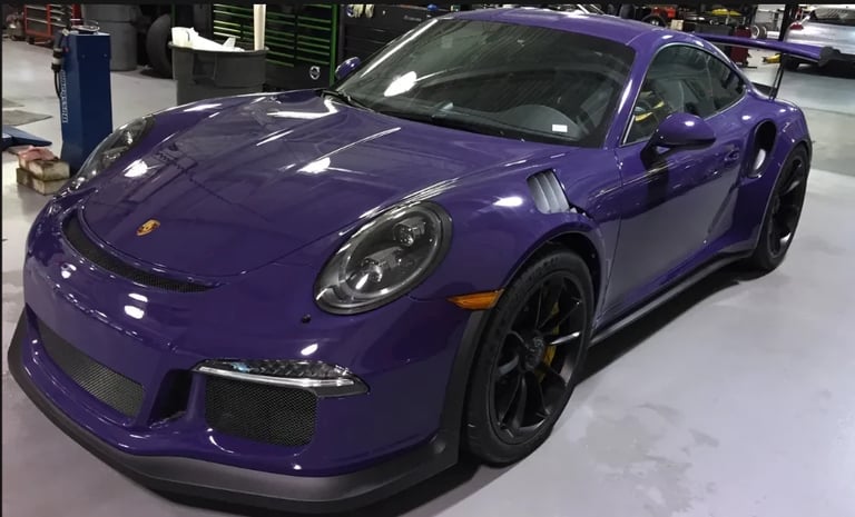 Purple Porsche 911 sports car displayed in a showroom with black wheels and glossy finish