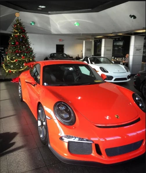 Bright red Porsche sports car on display in a luxury dealership showroom with Christmas tree and white sports car in background
