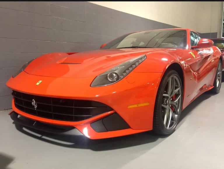 Bright red Ferrari sports car parked in a garage with gray walls, front three-quarter view