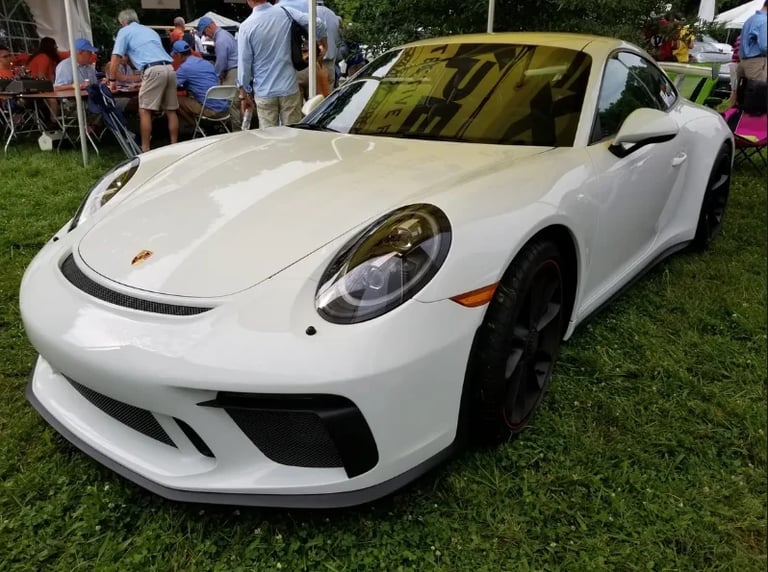 White Porsche 911 GT3 sports car displayed at an outdoor car show with spectators in the background