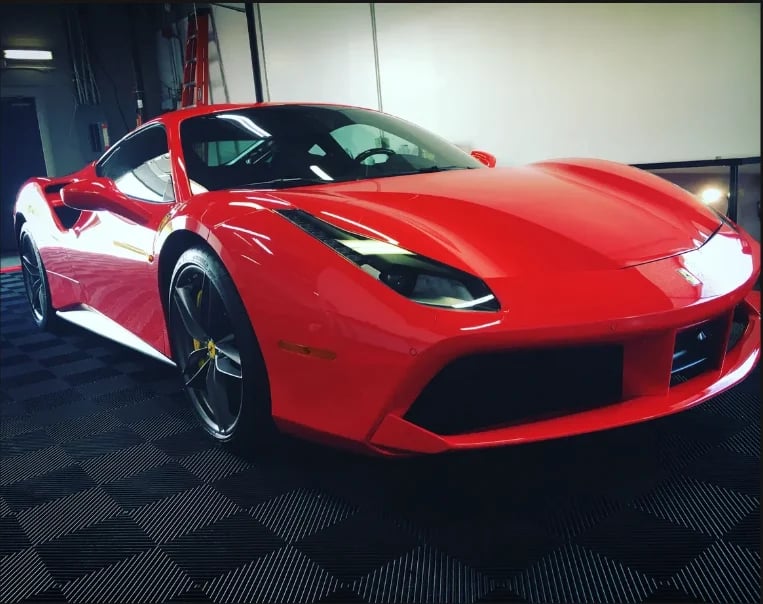 Bright red sports car with door open displayed in showroom with white walls and dark flooring