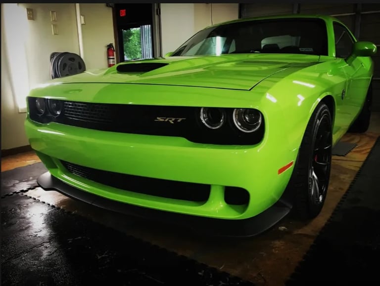 Bright green Dodge Challenger SRT muscle car with distinctive dual headlights parked in garage
